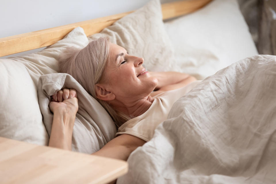 Middle-aged woman lying in bed smiling and stretching