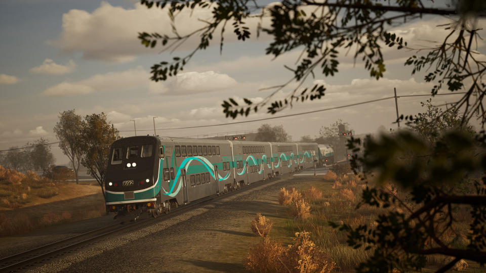 A train passing a tree under a cable line.