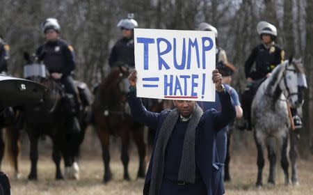 An anti-Trump protester holds his protest sign in front of mounted police outside a rally for Republican U.S. presidential candidate Donald Trump in Cleveland, Ohio, March 12, 2016. REUTERS/Rebecca Cook