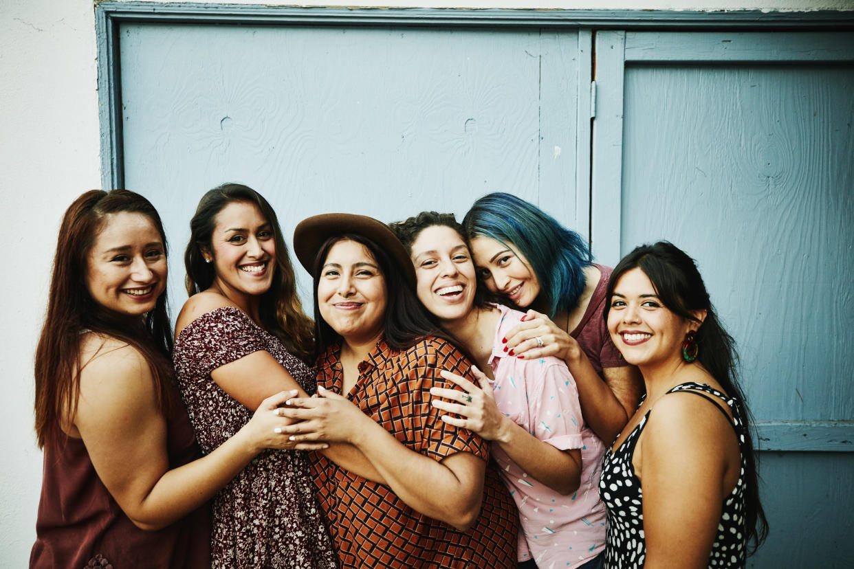 Portrait of female friends embracing in front of blue wall