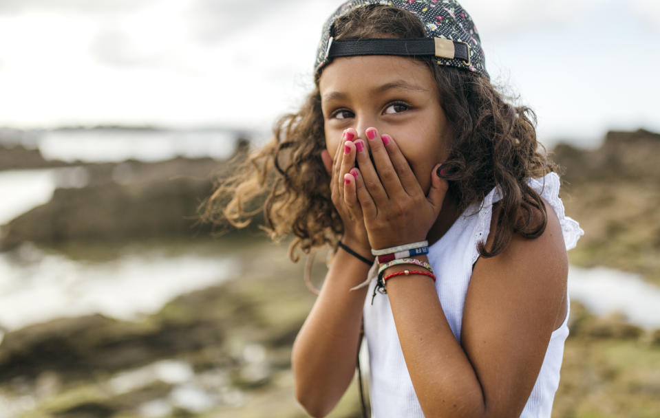 Girl covers mouth in surprise, outdoors with water in the background