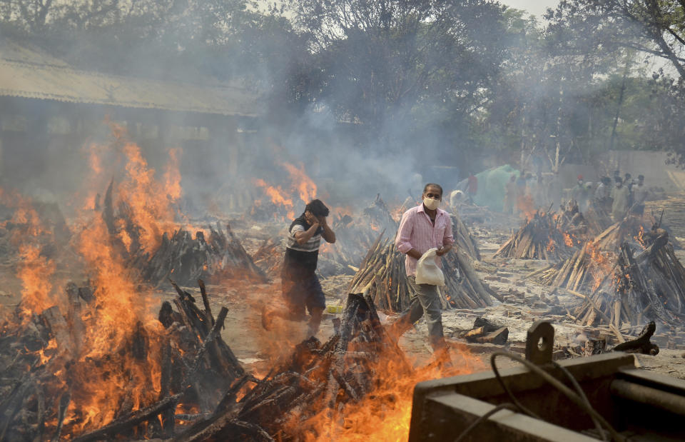 FILE - In this April 29, 2021, file photo, relatives react to heat emitting from the multiple funeral pyres of COVID-19 victims at a crematorium in the outskirts of New Delhi, India. COVID-19 infections and deaths are mounting with alarming speed in India with no end in sight to the crisis. People are dying because of shortages of bottled oxygen and hospital beds or because they couldn’t get a COVID-19 test. (AP Photo/Amit Sharma, File)