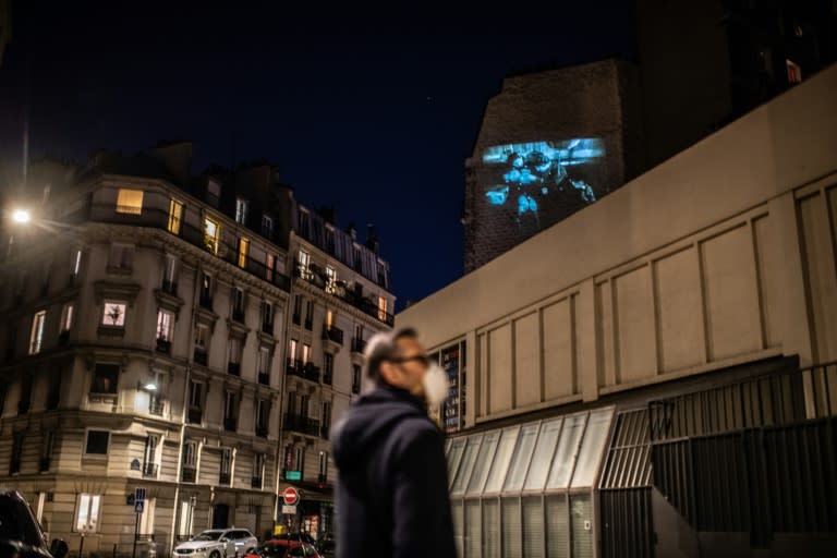 Un hombre con mascarilla visiona una película proyectada en la fachada del cine asociativo independiente La Clef de París el 1 de mayo de 2020, durante el confinamiento por el covid-19 (Martin Bureau)