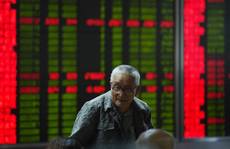 A Chinese investor looks at a share prices board in Beijing where rises are shown in red and losses in green
