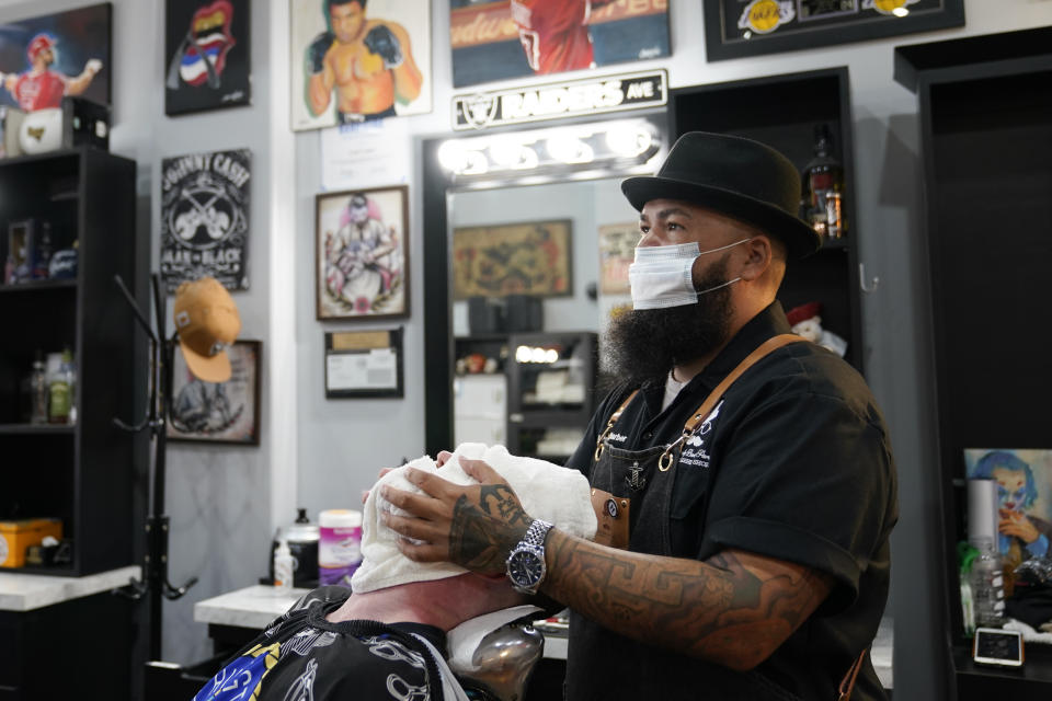 Luis Lopez, owner of Orange County Barbers Parlor, places a hot towel on Braunson McDonald on Wednesday, July 15, 2020, in Huntington Beach, Calif. Gov. Gavin Newsom this week ordered that indoor businesses like salons, barber shops, restaurants, movie theaters, museums and others close due to the spread of COVID-19. (AP Photo/Ashley Landis)