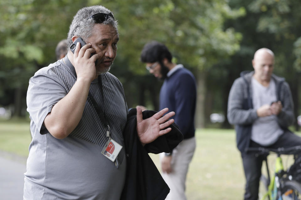 In this Friday March 15, 2019, photo, Al Noor mosque attack witness, Len Peneha, gestures as he describes events to The Associated Press on a mobile phone across a road from the mosque in central Christchurch, New Zealand. New Zealanders on Sunday, March 15, 2020, will commemorate those who died on the first anniversary of the mass killing, as the tragedy continues to ripple through the community. Three people whose lives were forever altered that day say it has prompted changes in their career aspirations, living situations and in the way that others perceive them. (AP Photo/Mark Baker)