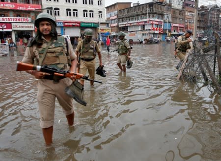 Central Reserve Police Force personnel carry their shoes as they wade through a water-logged street after heavy rain in Srinagar