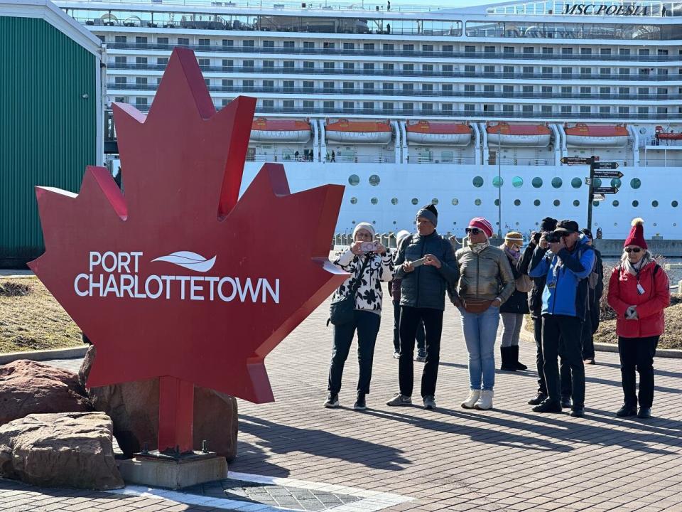 Tourists take photos of Port Charlottetown's sign as a cruise ship sits docked in harbour.