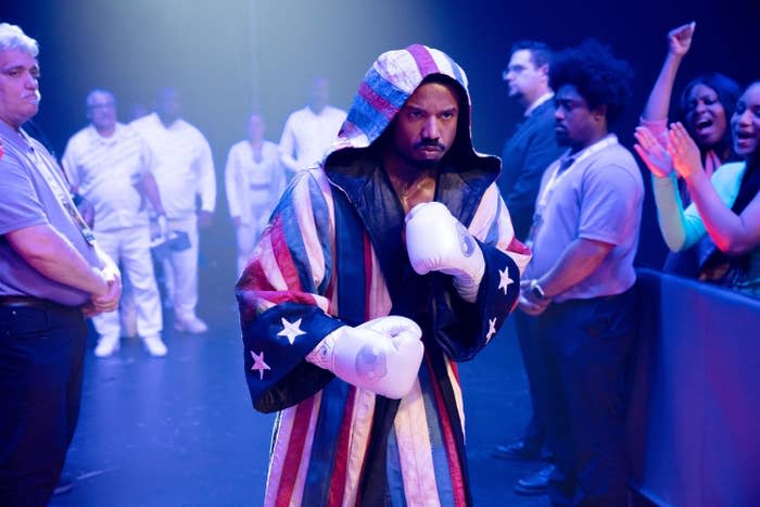 Adonis Creed, in his robe and boxing gloves, walks towards the ring as the spectators cheer