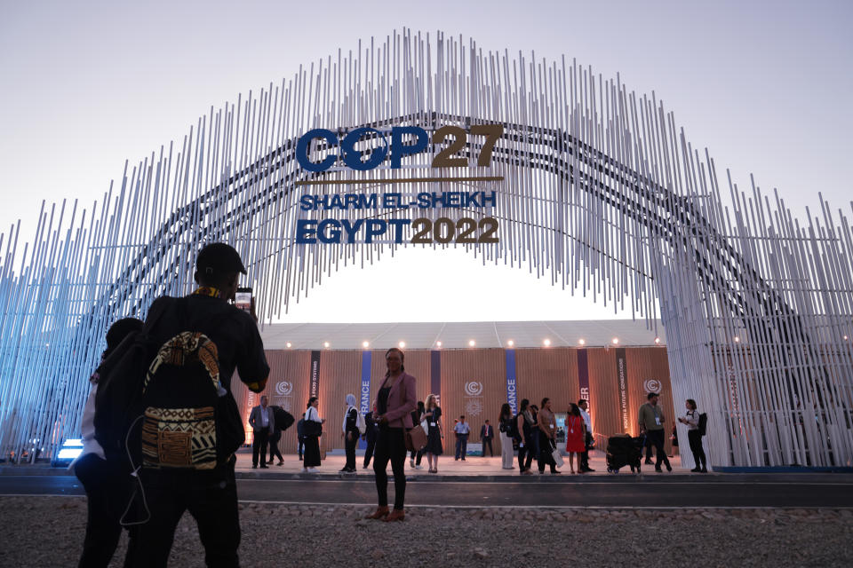 Attendees photograph one another near an arch that bears a sign reading: COP27, Sharm el-Sheikh, Egypt 2022.