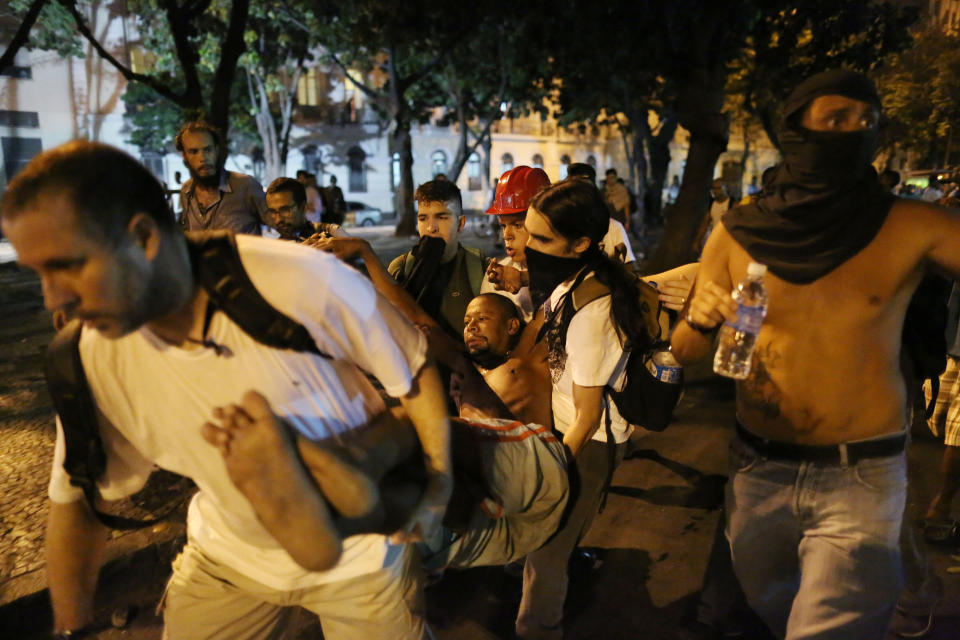 People carry a man injured in clashes with police when a protest against a bus fare increase turned violent in Rio de Janeiro, Brazil, Thursday, Feb. 6, 2014. Last year, millions of people took to the streets across Brazil complaining of higher bus fares, poor public services and corruption while the country spends billions on the World Cup, which is scheduled to start in June. (AP Photo/Leo Correa)