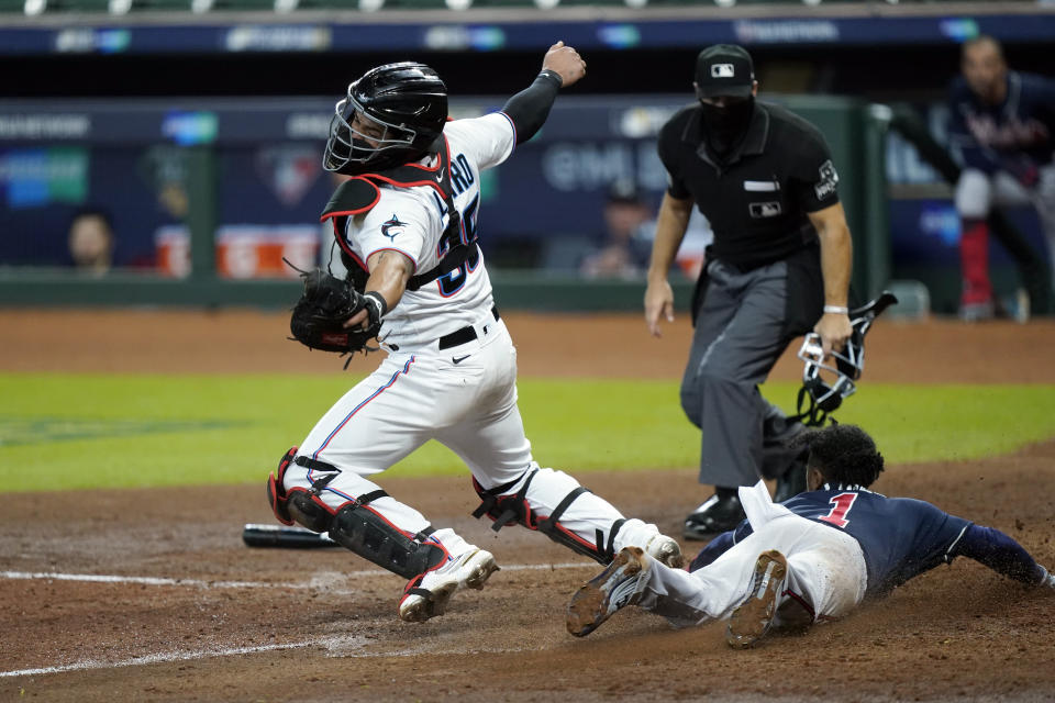 Atlanta Braves' Ozzie Albies (1) dives in to score on a hit by Dansby Swanson as Miami Marlins catcher Jorge Alfaro (38) reaches for the throw during the fifth inning in Game 3 of a baseball National League Division Series, Thursday, Oct. 8, 2020, in Houston. (AP Photo/David J. Phillip)