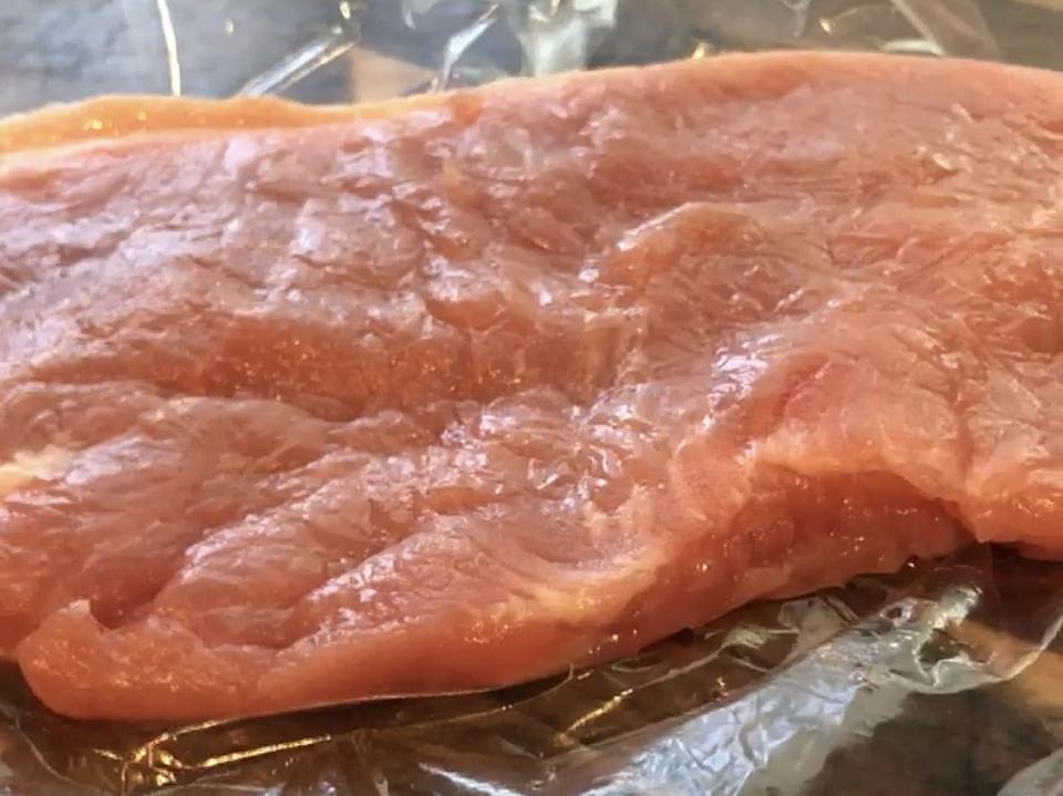 raw pork chop sitting on plastic bag over wooden cutting board