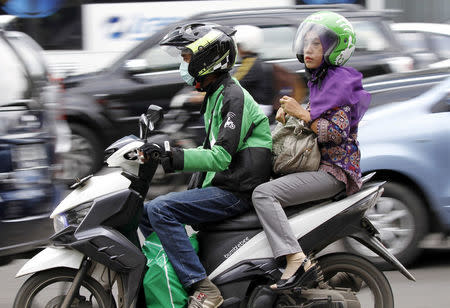 FILE PHOTO: A woman rides on the back of a motorbike, part of the Go-Jek ride-hailing service, on a busy street in central Jakarta, Indonesia December 18, 2015. REUTERS/Garry Lotulung/File Photo