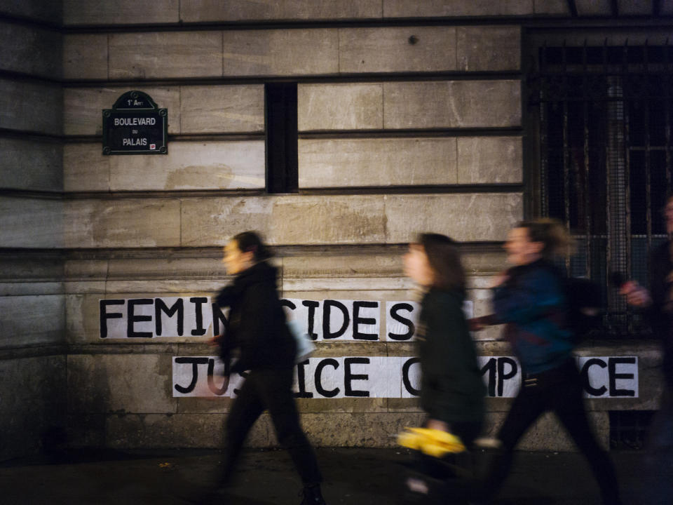 In this Nov. 4 2019 photo, Lea, Pauline and Clivia, from left, walk past a slogan they recently pasted on walls of the Palais de Justice courthouse reading " Femicides : guilty state, accomplice justice" in Paris. (AP Photo/Kamil Zihnioglu)