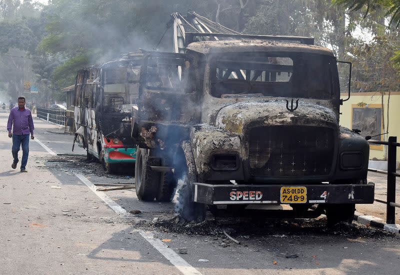 A man walks past damaged vehicles that were set on fire by demonstrators, during a protest after India's parliament passed Citizenship Amendment Bill, in Guwahati