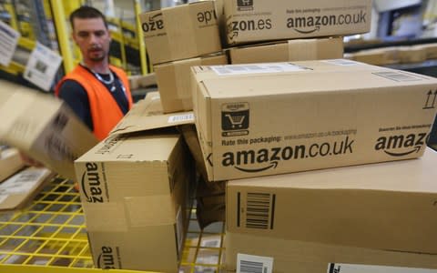 A worker in an orange high-vis jacket sorts through Amazon boxes that are piled on top of each other on yellow shelves. - Credit: Sean Gallup/Getty 