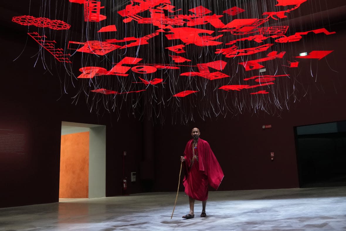 A man wearing traditional Masai clothes walks under an installation, at the Biennale International Architecture exhibition, in Venice, Italy, Wednesday, May 17, 2023. (AP Photo/Antonio Calanni)