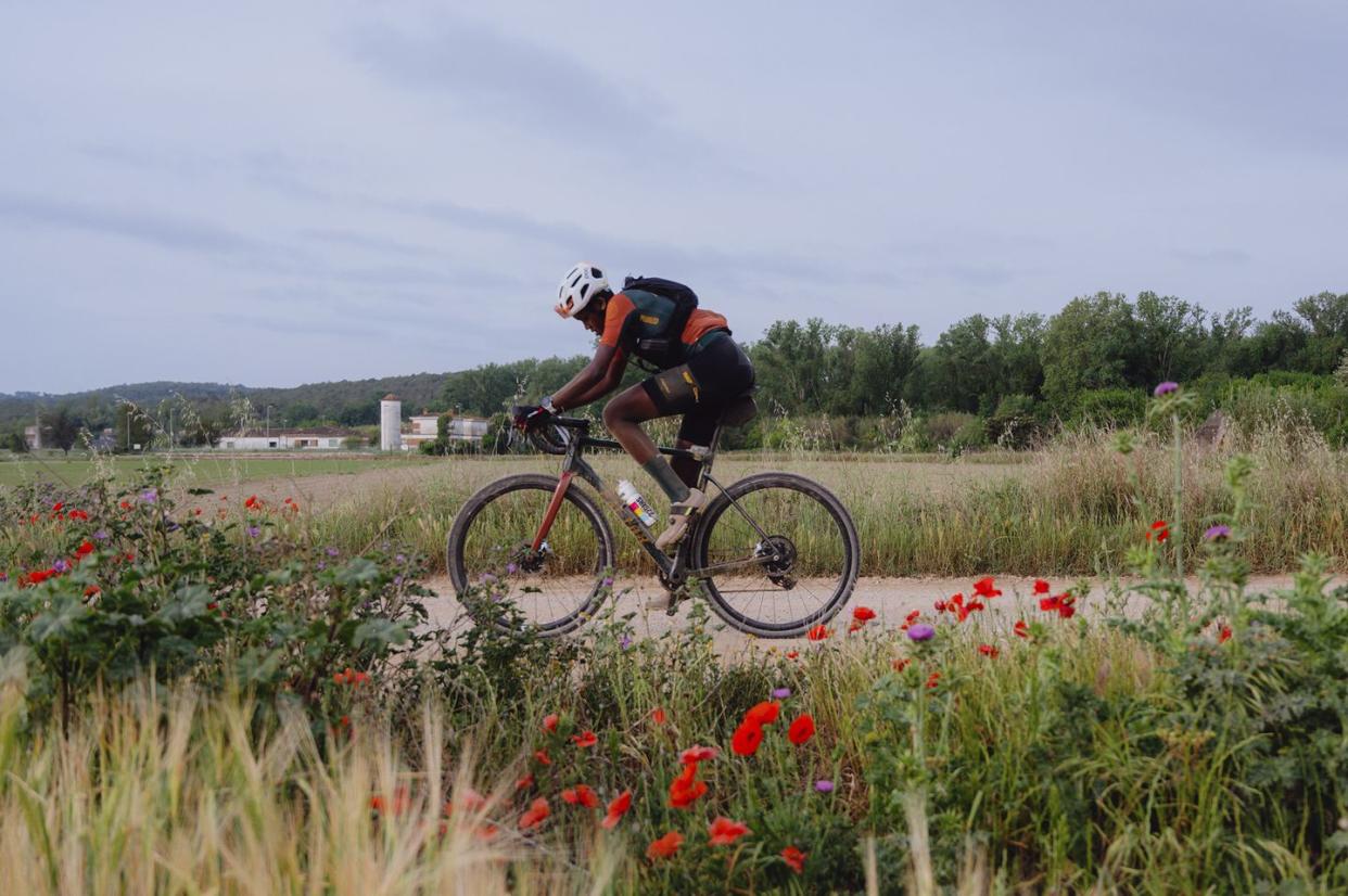 a cyclist rides past red flowers along a gravel road in girona spain