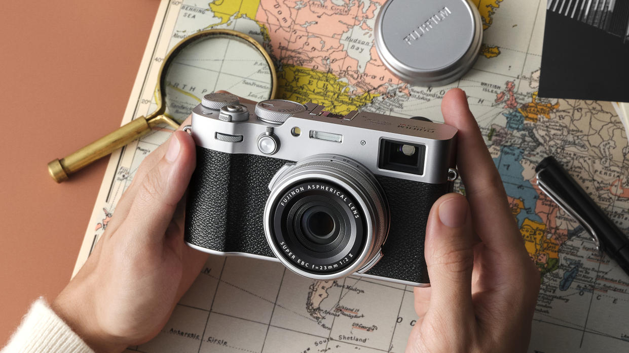  Fujifilm X100VI camera held between two hands over a map. 