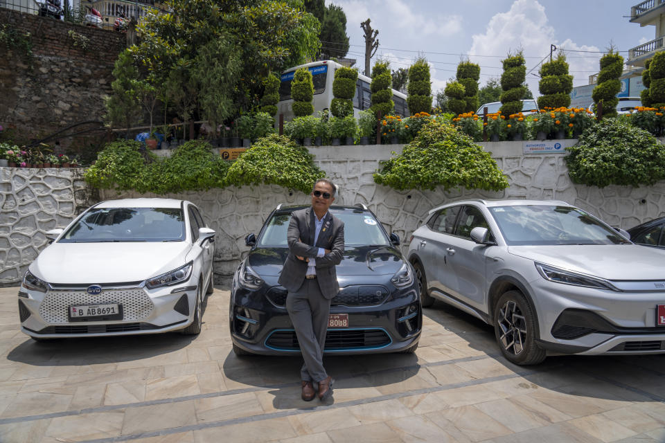 Jyotindra Sharma poses next to his electric car in Kathmandu, Nepal, Tuesday, May 14, 2024. Sharma, a cardiac surgeon who has been driving an EV, a 2019 KIA Niro, for four years, says he is glad to know he is helping reduce the smog that poses severe health hazards in the Kathmandu valley. (AP Photo/Niranjan Shrestha)