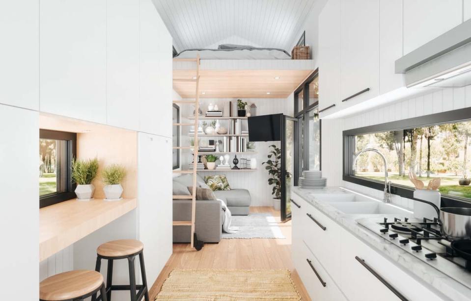 The white modern interior of a mobile home shows a a kitchen, sitting area, table, and bunk bed.