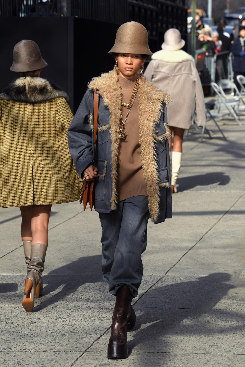 Model Lineisy Montero wears a denim shearling-lined jacket, baggy trousers, gold chunky jewelry, and platform boots for the ultimate hip-hop look