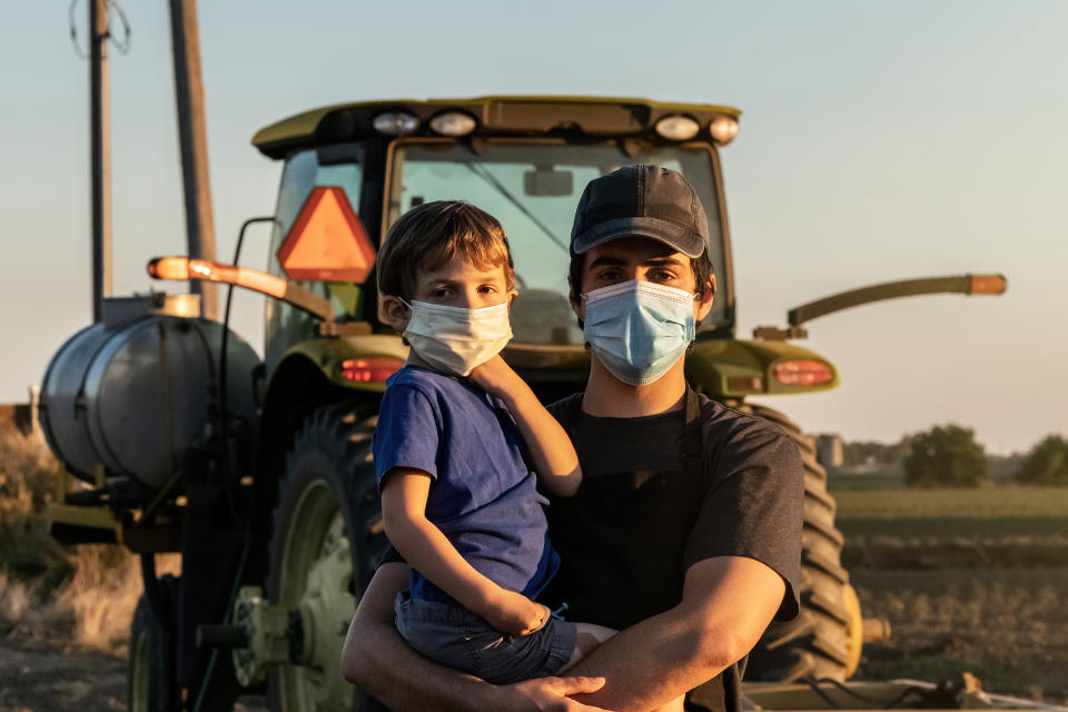 Young farmer posing with his son, both wearing protective face masks because COVID-19