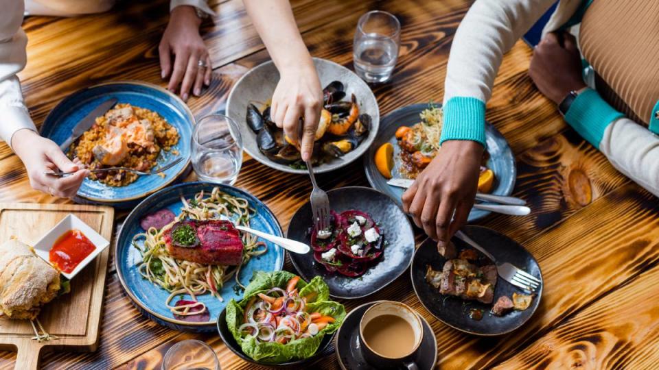 eat out for less: Unrecognisable friends sitting at a wooden table in a modern restaurant, enjoying a meal out together in Amble, North East England. They are all eating from the plates on the table.