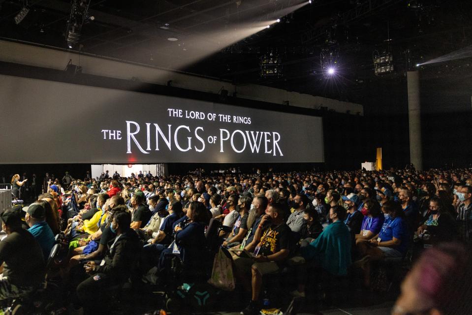 A packed room of people sitting in front of "The Rings of Power" screen