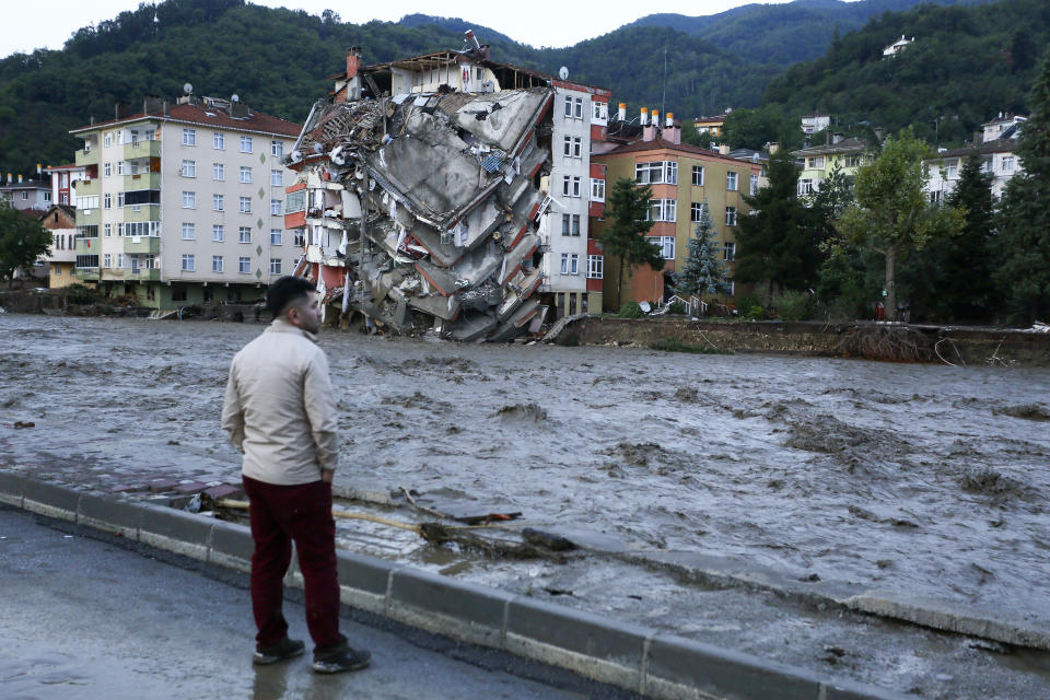 A man looks on as flood waters sweep by in Bozkurt town of Kastamonu province of Turkey, Thursday, Aug. 12, 2021. The floods triggered by torrential rains battered the Black Sea coastal provinces of Bartin, Kastamonu, Sinop and Samsun on Wednesday, demolishing homes and bridges and sweeping cars away by torrents. Helicopters scrambled to rescue people stranded on rooftops.(IHA via AP)