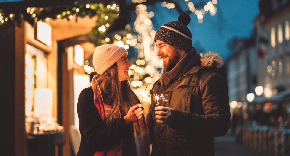 A man and a woman look in love as they stand on a street holding Christmas sparklers and are dressed in winter clothes. (Getty Images)