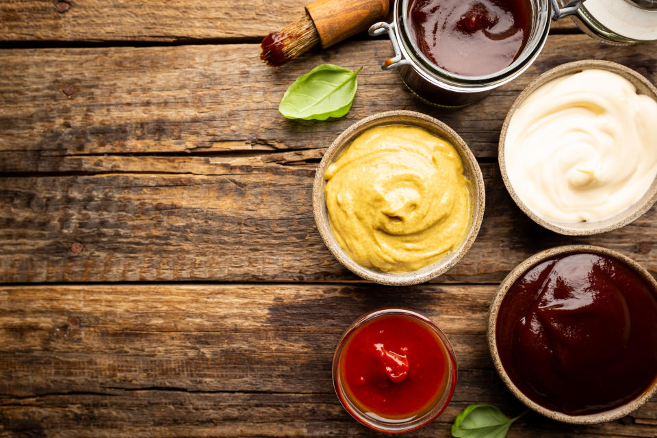 Classic set of sauces, American yellow mustard, ketchup, barbecue sauce, mayonnaise on wooden background, top view with copy space.