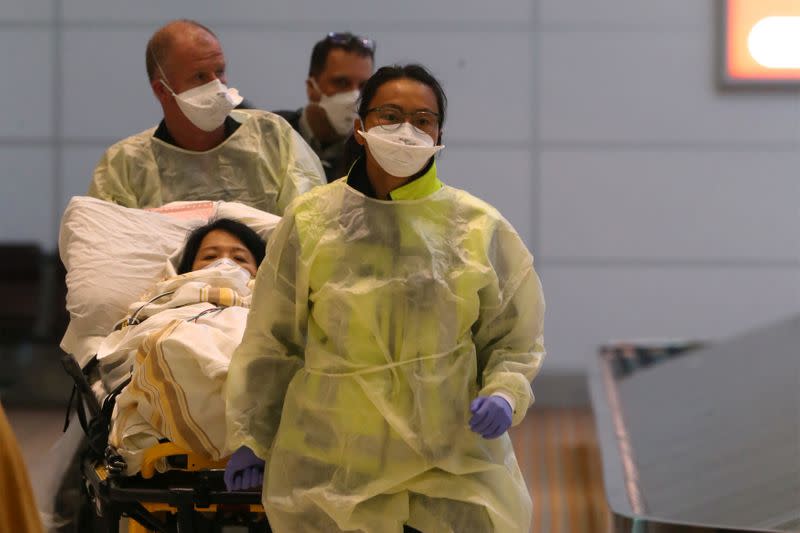 Paramedics dressed in protective clothing and wearing masks guide a stretcher carrying an ill woman in Winnipeg airport