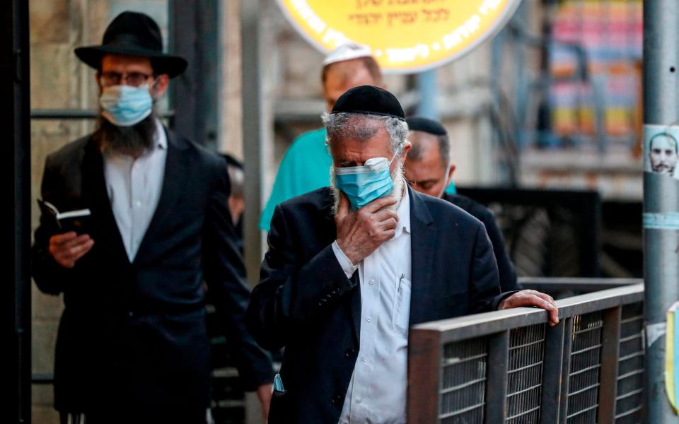 Orthodox Jewish men, mask-clad due to the COVID-19 coronavirus pandemic, pray along a sidewalk in Jerusalem - AFP