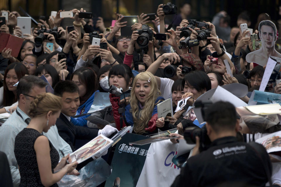 In this Monday, March 24, 2014 photo, fans watch actress Scarlett Johansson, left in foreground, sign her autograph during a publicity event ahead of the April release of her movie "Captain America: The Winter Soldier" in Beijing. Captain America and Spiderman are seeking to dominate the Chinese box office in the coming weeks, proving that U.S. patriotic superheroes can overcome China’s leeriness of foreign films if they promise big money. Chinese authorities, wary of outside cultural influences and competition, restrict the number of foreign movies shown in the mainland’s cinemas to 34 each year. (AP Photo/Ng Han Guan)