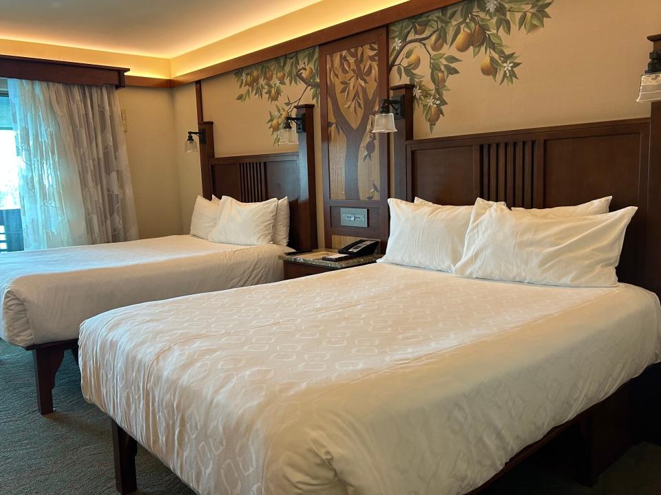 A hotel room with two queen beds with white linens and a mural of a pear tree on the wall.