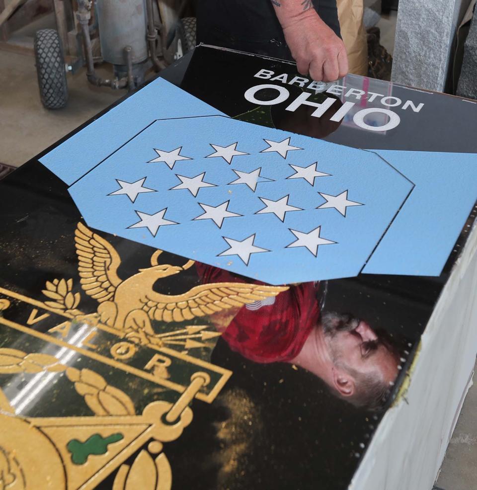 The reflection of Ken Noon, the owner of Summit Memorials, is seen on the granite memorial he is making to honor WWII war hero Howard Woodford that will be dedicated on Memorial Day in Barberton.