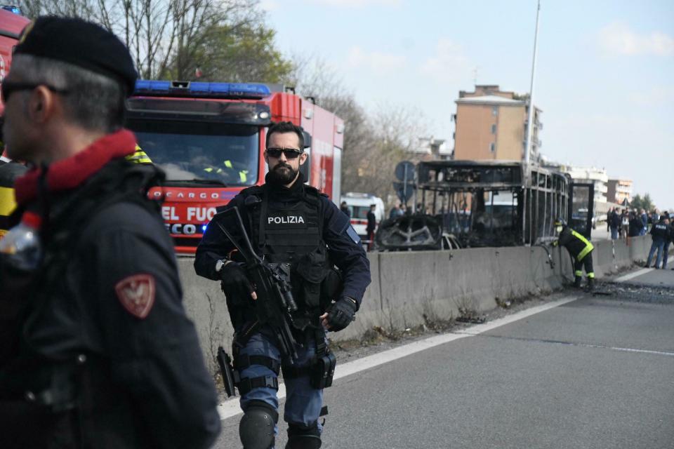 Firefighters and police officers stand by the gutted remains of a bus in San Donato Milanese, near Milan, Italy, March 21, 2019. Italian authorities say a bus driver transporting schoolchildren stopped his vehicle on a provincial highway, told the passengers to get off and then doused the interior with gasoline and set it on fire. Italian media reported that the driver, an Italian of Senegalese origin, was immediately apprehended. (Daniele Bennati/ANSA via AP)