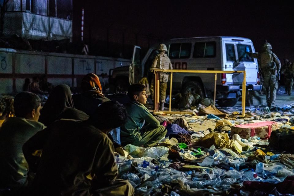 Afghan refugees sit on the ground in a group as British military secure the perimeter outside the Baron Hotel