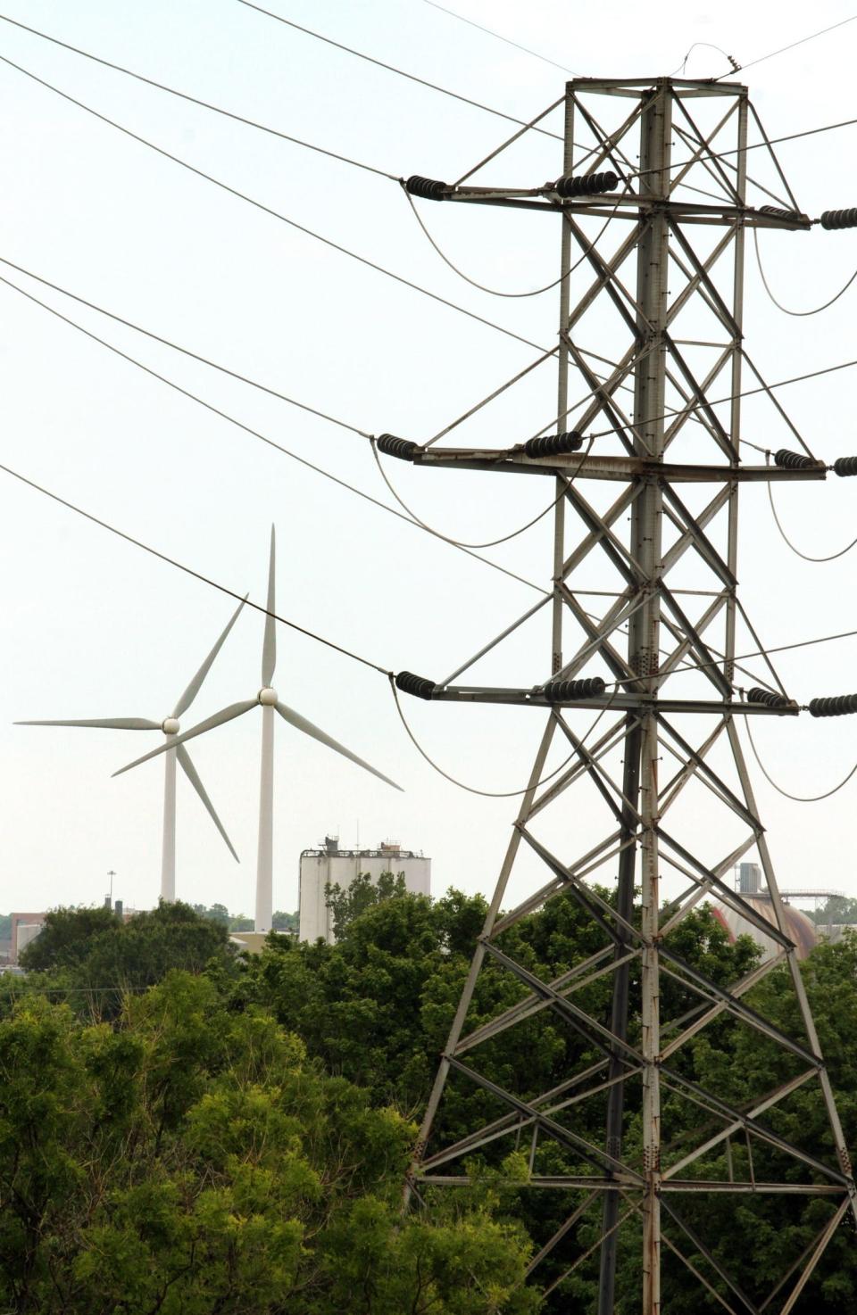 Transmission lines are pictured in Rhode Island, with the Narragansett Bay Commission's wind turbines in the background.