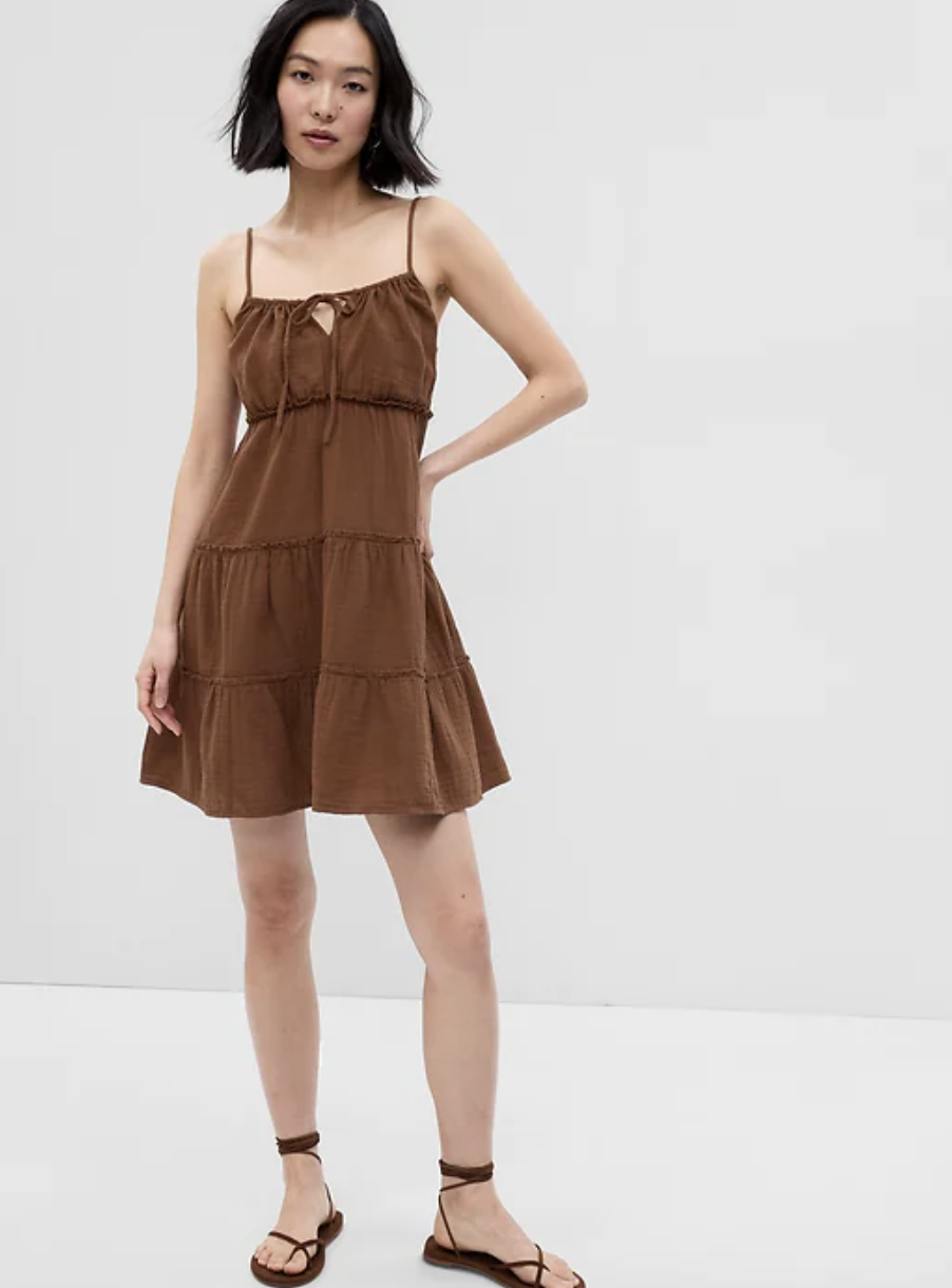 asian model wearing sandals and Crinkle Gauze Tiered Mini Dress in Medium Warm Brown (photo via Gap)