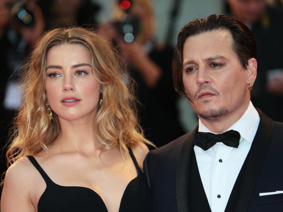 Amber and Johnny in black formal ensembles posing and looking with stern faces.