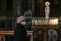 A woman wearing a mask walks past candles at the Santa Maria ai Monti church, in Rome Sunday, March 29, 2020. The new coronavirus causes mild or moderate symptoms for most people, but for some, especially older adults and people with existing health problems, it can cause more severe illness or death. (Cecilia Fabiano/LaPresse via AP)