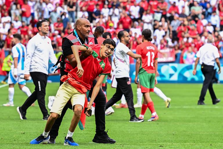 A member of security holds a fan of Morocco after numerous Morocco's fans invaded the pitch at the end of the men's group B football match between Argentina and Morocco during the Paris 2024 Olympic Games at the Geoffroy-Guichard Stadium in Saint-Etienne on July 24, 2024. (Photo by Arnaud FINISTRE / AFP)