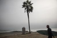 A bird perches on a public bathroom while a surfer walks toward the Pacific Ocean on the coast of Lima, Peru, Friday, June 26, 2020. The emblematic surfers who dot Peru's coastline are retaking to the waves as the hard-hit nation relaxes coronavirus-related restrictions on outdoor sports. (AP Photo/Rodrigo Abd)