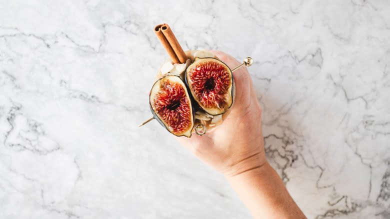 hand holding smoothie garnished with figs on skewer, almonds and cinnamon