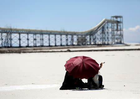 A couple rests near the industrial plant for potassium chloride, a product that is extracted from brine under a programme developed by Bolivia to produce lithium, in Llipi, on the salt lake of Uyuni, Potosi, Bolivia, October 7, 2018, REUTERS/David Mercado