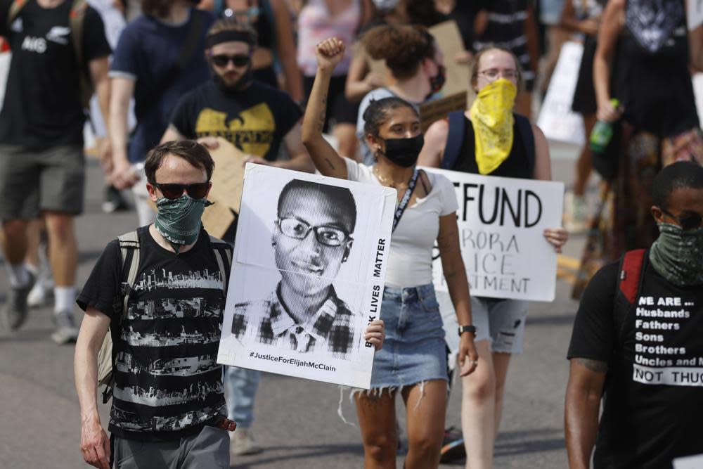 In this June 27, 2020 file photo, demonstrators carry placards as they walk down Sable Boulevard during a rally and march over the death of Elijah McClain in Aurora, Colo. (AP Photo/David Zalubowski, File)