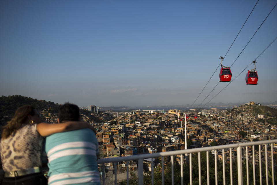 In this May 10, 2013 photo, a couple looks out over the the Complexo do Alemao slum where cable-cars move commuters above the homes in Rio de Janeiro, Brazil. The cable-car system linking six of Alemao's hilltops over a 3.5-kilometer (2.3-mile) route has become a popular tourist attraction. (AP Photo/Felipe Dana)